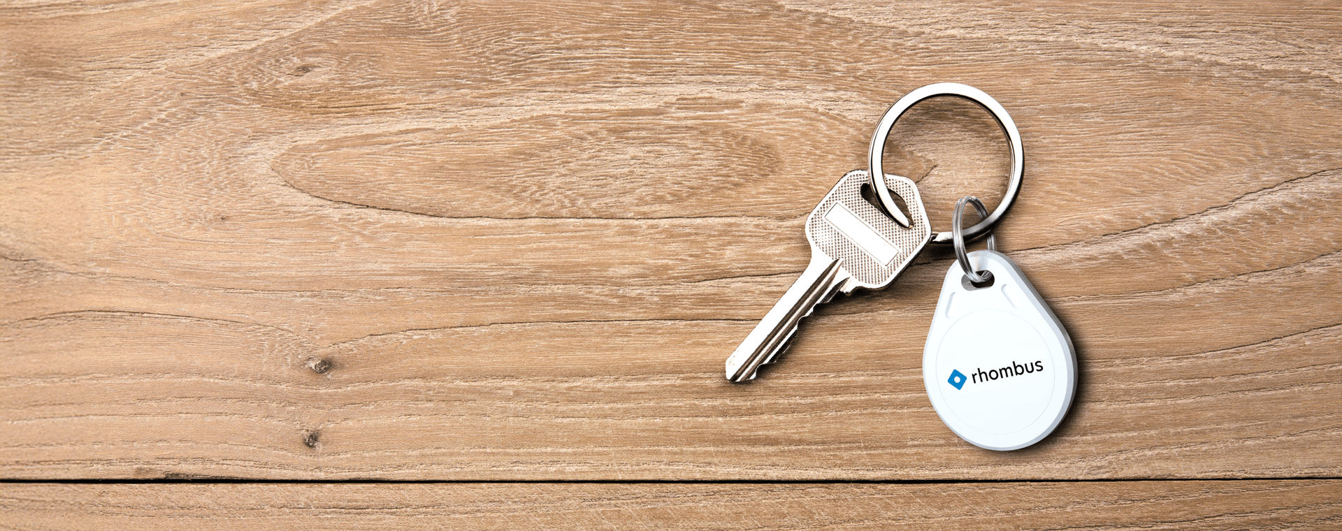 A white key fob featuring the word "Rhombus" in bold text and key chain  set against a wood background.